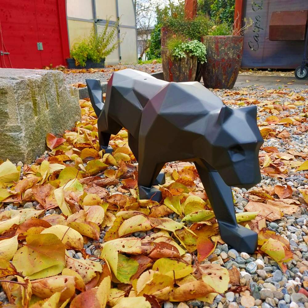 Sleek matte black polygonal panther sculpture crafted from welded steel, posed on autumn leaves